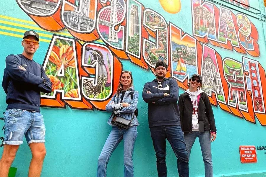 Visitantes de moda posan frente a un mural de San Francisco.