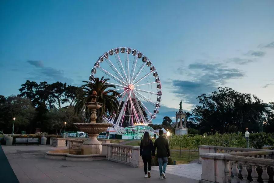 A couple walks toward the SkyStar Ferris Wheel at dusk.