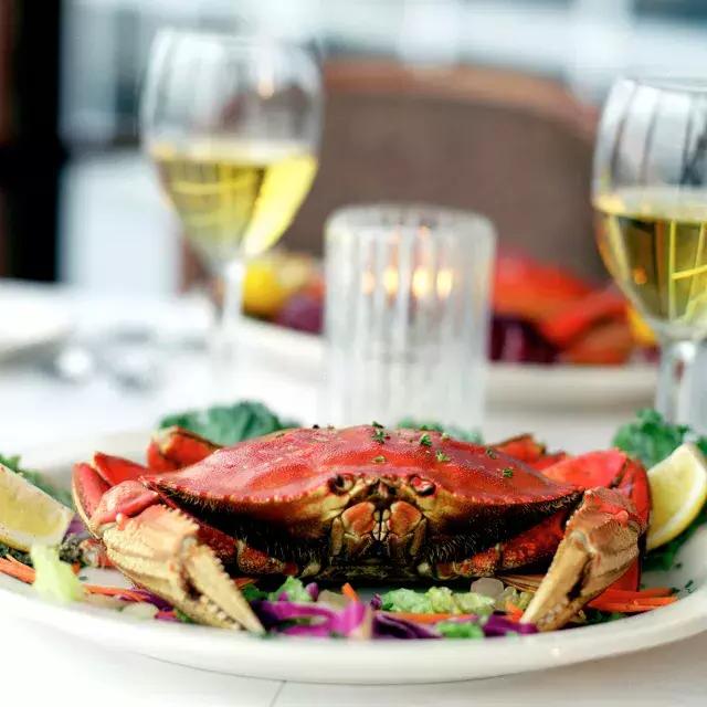 一只奇葩螃蟹就在餐厅的盘子里, 背景里有两杯白葡萄酒.
